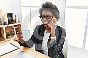 Young african american woman speaking on the phone drinking coffee at office