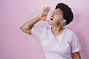 Young african american woman standing over pink background shouting and screaming loud to side with hand on mouth