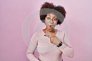Young african american woman standing over pink background surprised pointing with finger to the side, open mouth amazed