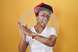 Young african american woman standing over yellow background clapping and applauding happy and joyful, smiling proud hands