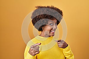 Young african american woman standing over yellow background pointing fingers to camera with happy and funny face