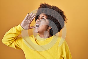 Young african american woman standing over yellow background shouting and screaming loud to side with hand on mouth
