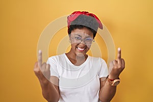 Young african american woman standing over yellow background showing middle finger doing fuck you bad expression, provocation and