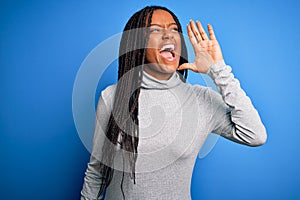 Young african american woman standing wearing casual turtleneck over blue isolated background shouting and screaming loud to side