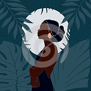 Young African American woman stands against the backdrop of the moon. Night in the jungle. Large tropical leaves
