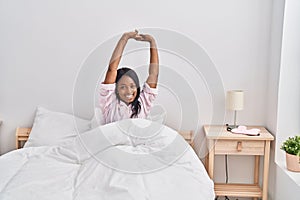 Young african american woman stretching arms sitting on bed at bedroom
