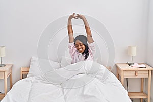 Young african american woman stretching arms sitting on bed at bedroom