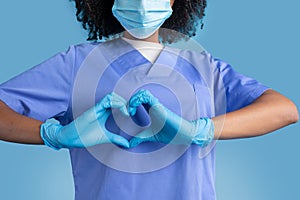 Young african american woman surgeon, doctor, nurse in blue uniform, protective mask, gloves making heart sign