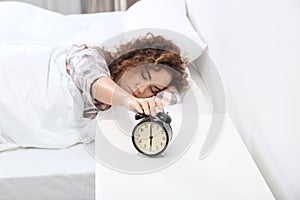 Young African-American woman turning off alarm clock at home.