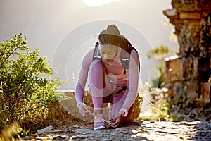 Young african american woman tying the laces of her sneakers for exercise outdoors. One female only fastening and