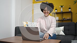Young african american woman using laptop sitting on sofa at home