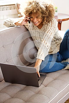 Young african american woman using mobile and looking at laptop computer
