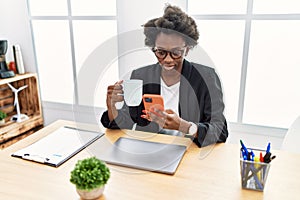 Young african american woman using smartphone drinking coffee at office