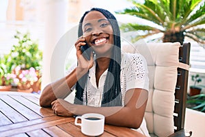 Young african american woman using smartphone and drinking coffee at terrace