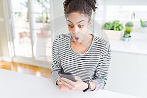 Young african american woman using smartphone texting a message scared in shock with a surprise face, afraid and excited with fear