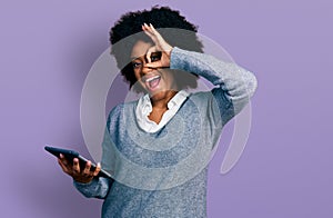 Young african american woman using touchpad device smiling happy doing ok sign with hand on eye looking through fingers