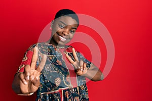 Young african american woman wearing african style smiling looking to the camera showing fingers doing victory sign