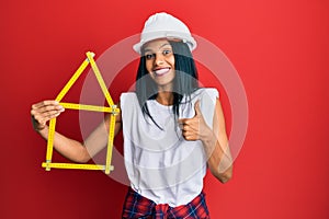 Young african american woman wearing architect hardhat holding build project smiling happy and positive, thumb up doing excellent