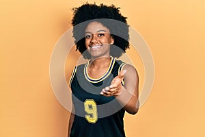 Young african american woman wearing basketball uniform smiling friendly offering handshake as greeting and welcoming