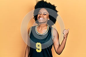 Young african american woman wearing basketball uniform smiling with happy face looking and pointing to the side with thumb up