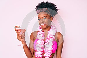 Young african american woman wearing bikini and hawaiian lei holding cocktail looking positive and happy standing and smiling with