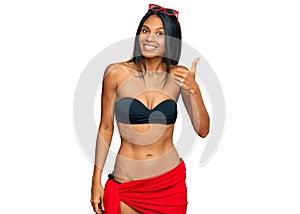 Young african american woman wearing bikini smiling with happy face looking and pointing to the side with thumb up