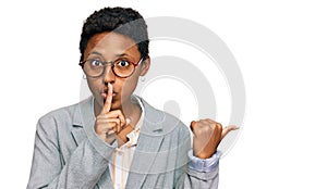 Young african american woman wearing business clothes asking to be quiet with finger on lips pointing with hand to the side