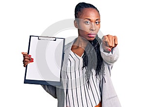 Young african american woman wearing business clothes holding clipboard pointing with finger to the camera and to you, confident