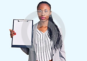 Young african american woman wearing business clothes holding clipboard thinking attitude and sober expression looking self