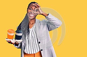 Young african american woman wearing business clothes holding take away cup of coffee smiling happy doing ok sign with hand on eye