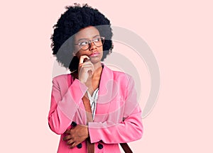 Young african american woman wearing business clothes and leather bag serious face thinking about question with hand on chin,