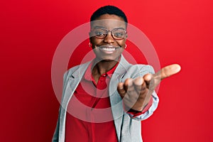 Young african american woman wearing business jacket and glasses smiling friendly offering handshake as greeting and welcoming