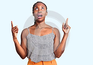 Young african american woman wearing casual clothes amazed and surprised looking up and pointing with fingers and raised arms