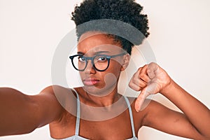 Young african american woman wearing casual clothes and glasses making selfie by the camera with angry face, negative sign showing