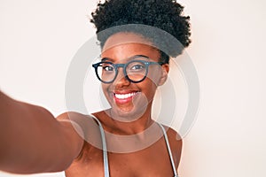 Young african american woman wearing casual clothes and glasses making selfie by the camera looking positive and happy standing