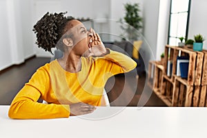 Young african american woman wearing casual clothes sitting on the table at home shouting and screaming loud to side with hand on