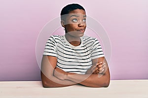 Young african american woman wearing casual clothes sitting on the table smiling looking to the side and staring away thinking