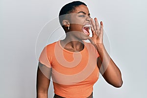 Young african american woman wearing casual orange t shirt shouting and screaming loud to side with hand on mouth