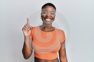 Young african american woman wearing casual orange t shirt showing and pointing up with finger number one while smiling confident