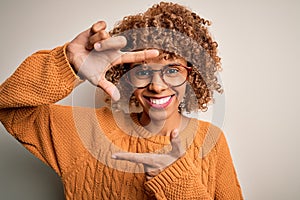 Young african american woman wearing casual sweater and glasses over white background smiling making frame with hands and fingers