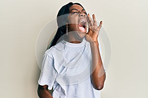 Young african american woman wearing casual white t shirt shouting and screaming loud to side with hand on mouth