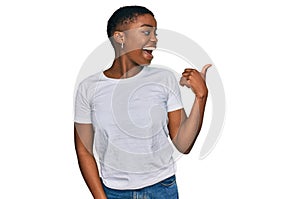 Young african american woman wearing casual white t shirt smiling with happy face looking and pointing to the side with thumb up