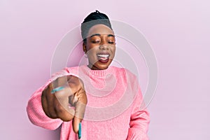 Young african american woman wearing casual winter sweater laughing at you, pointing finger to the camera with hand over body,