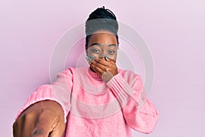 Young african american woman wearing casual winter sweater laughing at you, pointing finger to the camera with hand over mouth,