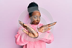 Young african american woman wearing casual winter sweater rejection expression crossing arms and palms doing negative sign, angry