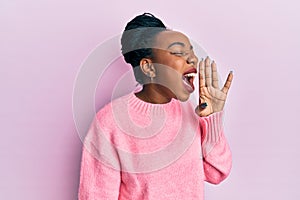 Young african american woman wearing casual winter sweater shouting and screaming loud to side with hand on mouth