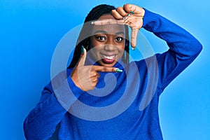 Young african american woman wearing casual winter sweater smiling making frame with hands and fingers with happy face