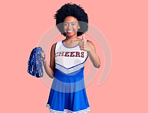 Young african american woman wearing cheerleader uniform holding pompom approving doing positive gesture with hand, thumbs up