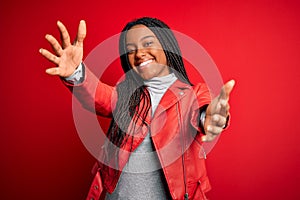 Young african american woman wearing cool fashion leather jacket over red  background looking at the camera smiling with