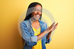 Young african american woman wearing denim shirt standing over isolated yellow background clapping and applauding happy and